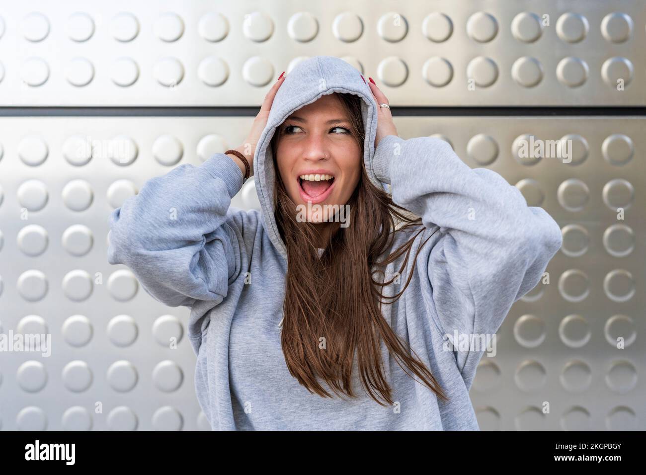 Femme avec la bouche ouverte portant une chemise à capuchon devant un mur en métal Banque D'Images