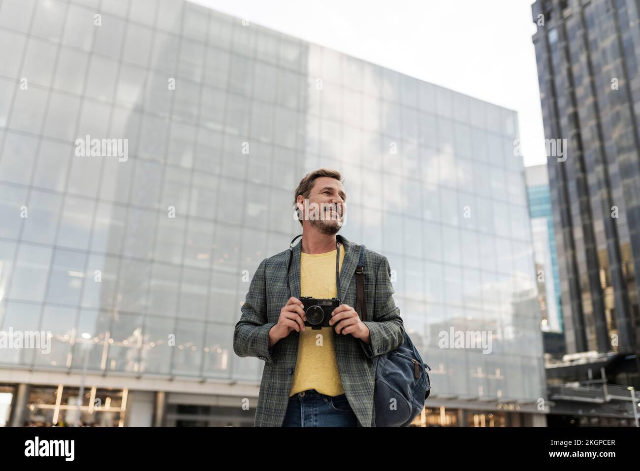 Homme souriant avec caméra devant le bâtiment Banque D'Images