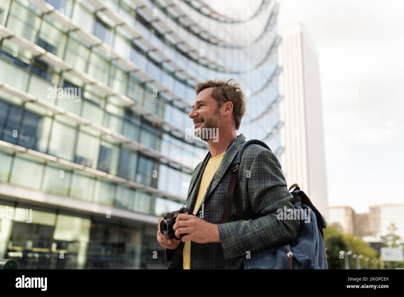 Homme souriant avec caméra devant le bâtiment Banque D'Images