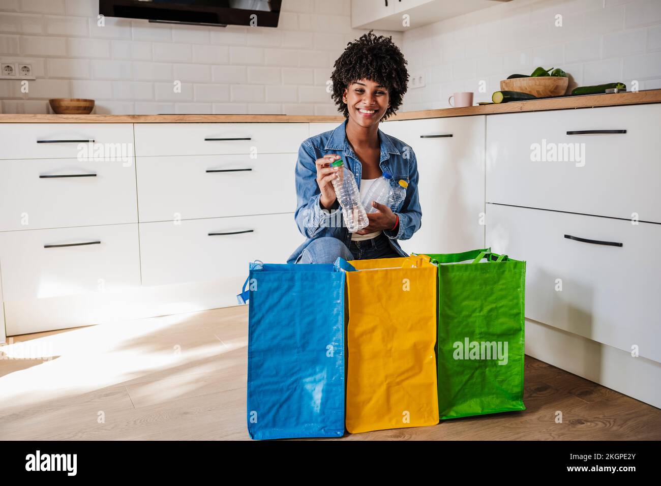 Bonne jeune femme recyclant les bouteilles en plastique dans des sacs réutilisables Banque D'Images
