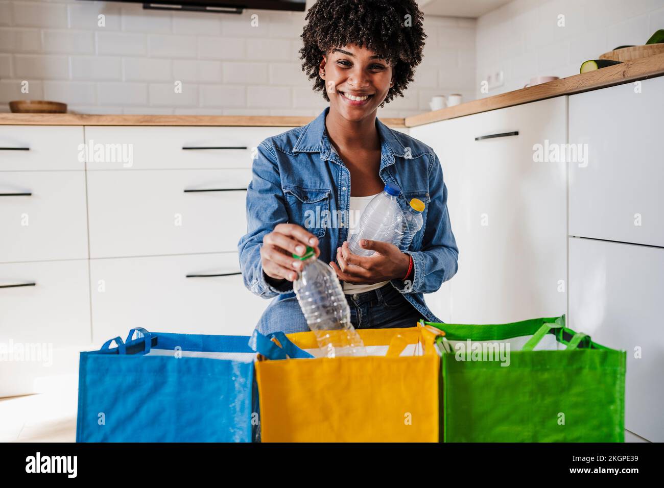 Bonne femme recyclant des bouteilles en plastique dans des sacs réutilisables à la maison Banque D'Images