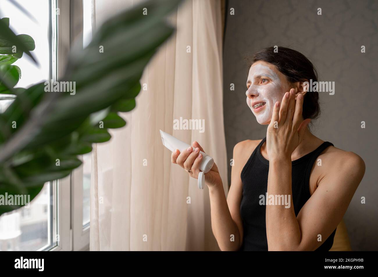 Femme réfléchie appliquant un masque de soin de la peau sur le visage à la maison Banque D'Images