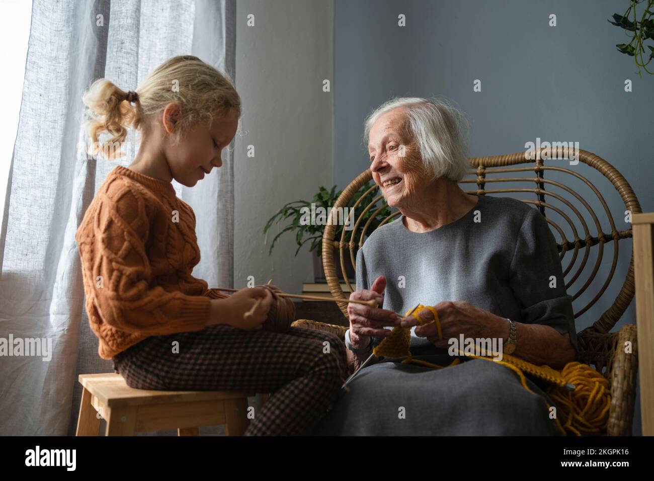 Femme aînée souriante regardant la petite-fille tenant une aiguille tricotage dans le salon Banque D'Images
