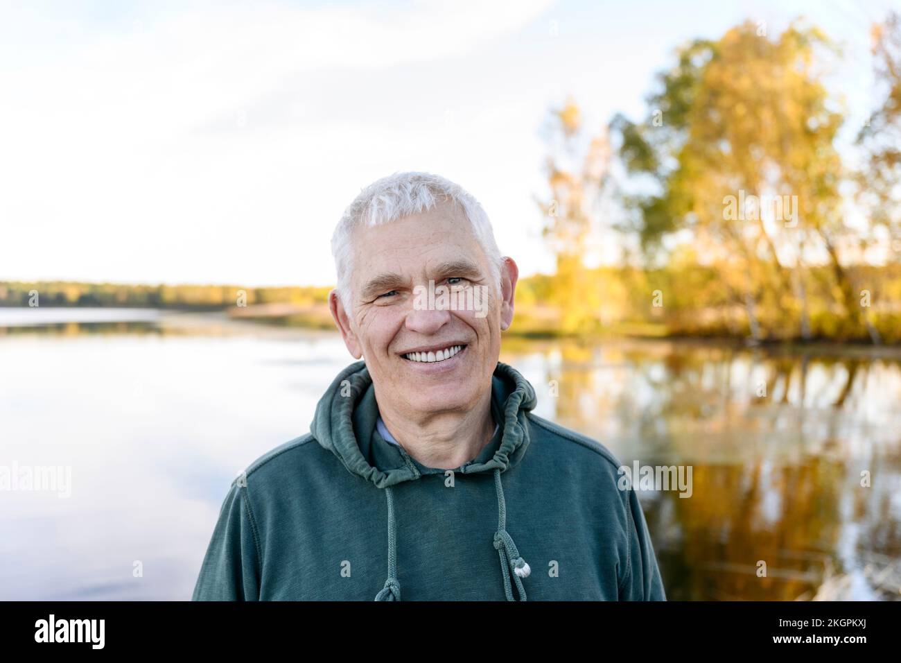 Homme senior souriant en face du lac Banque D'Images