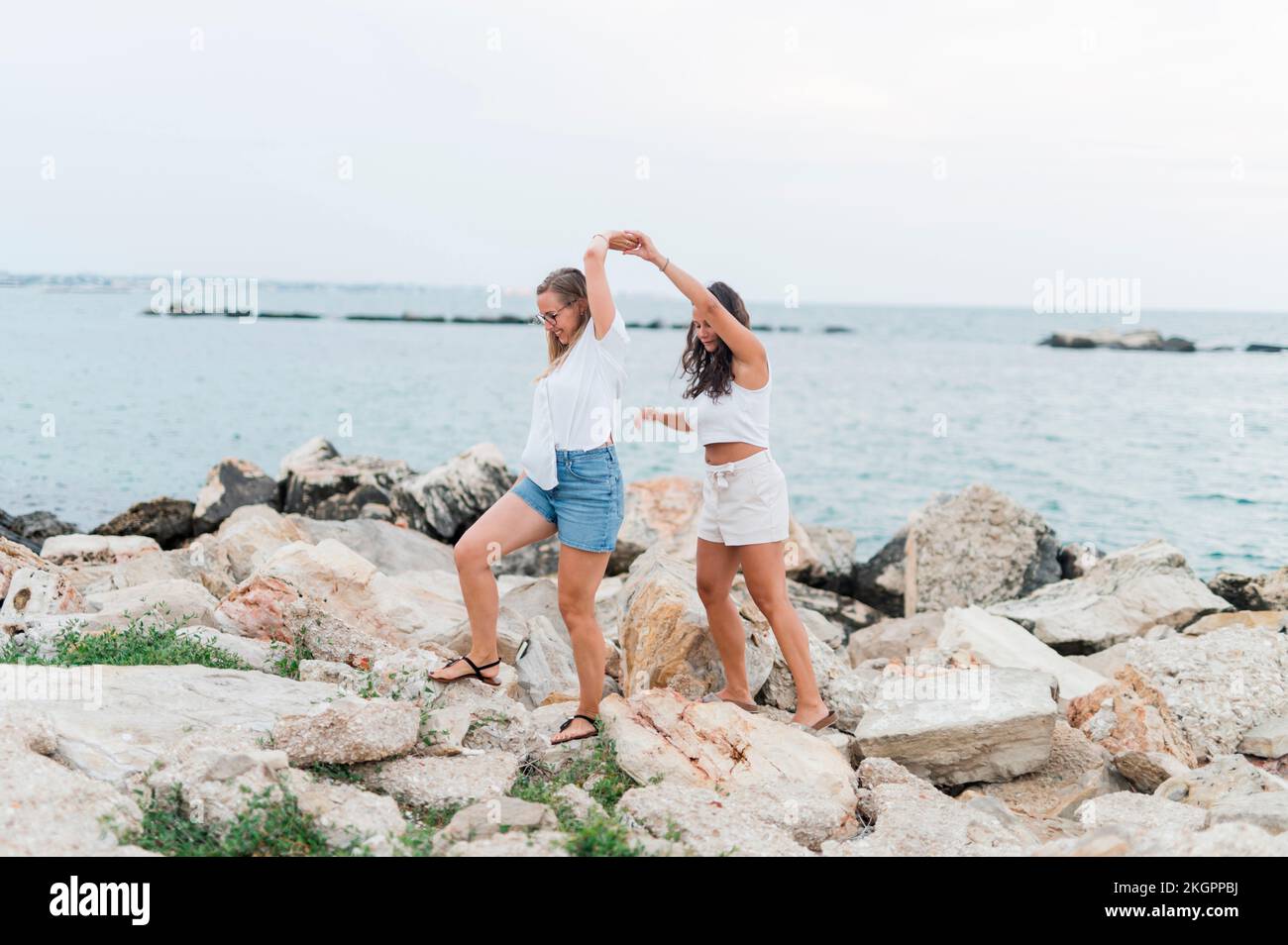 Des amis se tenant les mains et marchant ensemble sur le rocher à la plage Banque D'Images Des amis se tenant les mains et marchant ensemble sur le rocher à la plage Banque D'Images