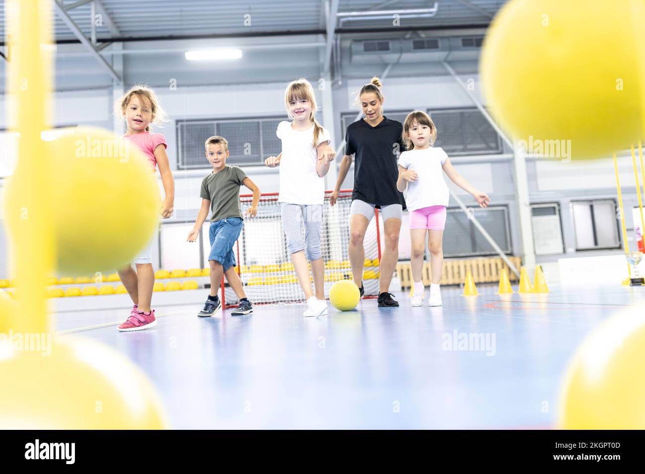 L'enseignement des enseignants donne des coups de pied aux élèves avec du ballon sur le terrain de sport de l'école Banque D'Images