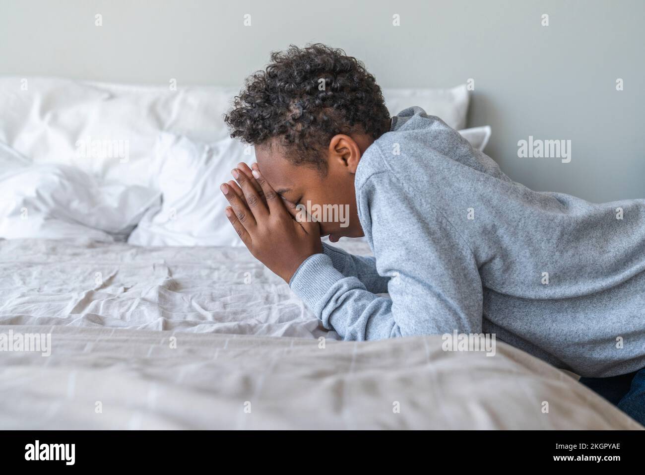 Garçon avec les mains classed sur le lit à la maison Banque D'Images