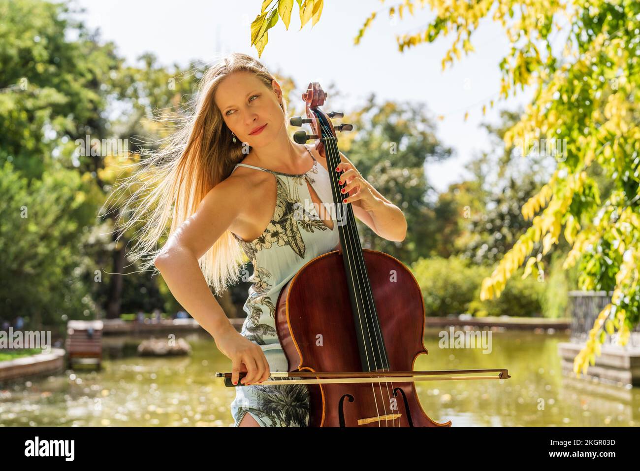 Femme blonde jouant du violoncelle devant le lac au parc Banque D'Images