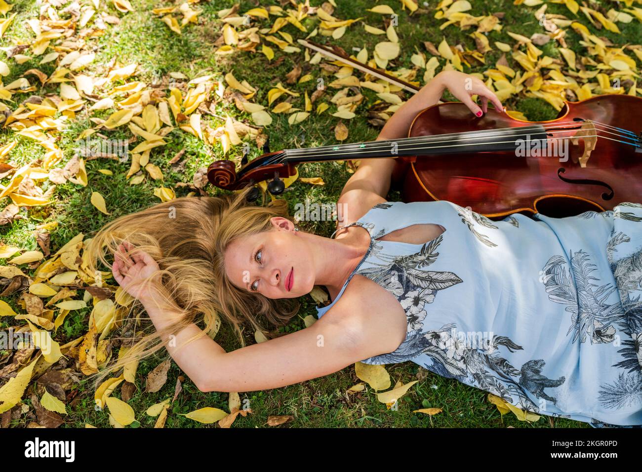 Femme blonde couchée sur l'herbe avec violoncelle dans le parc Banque D'Images
