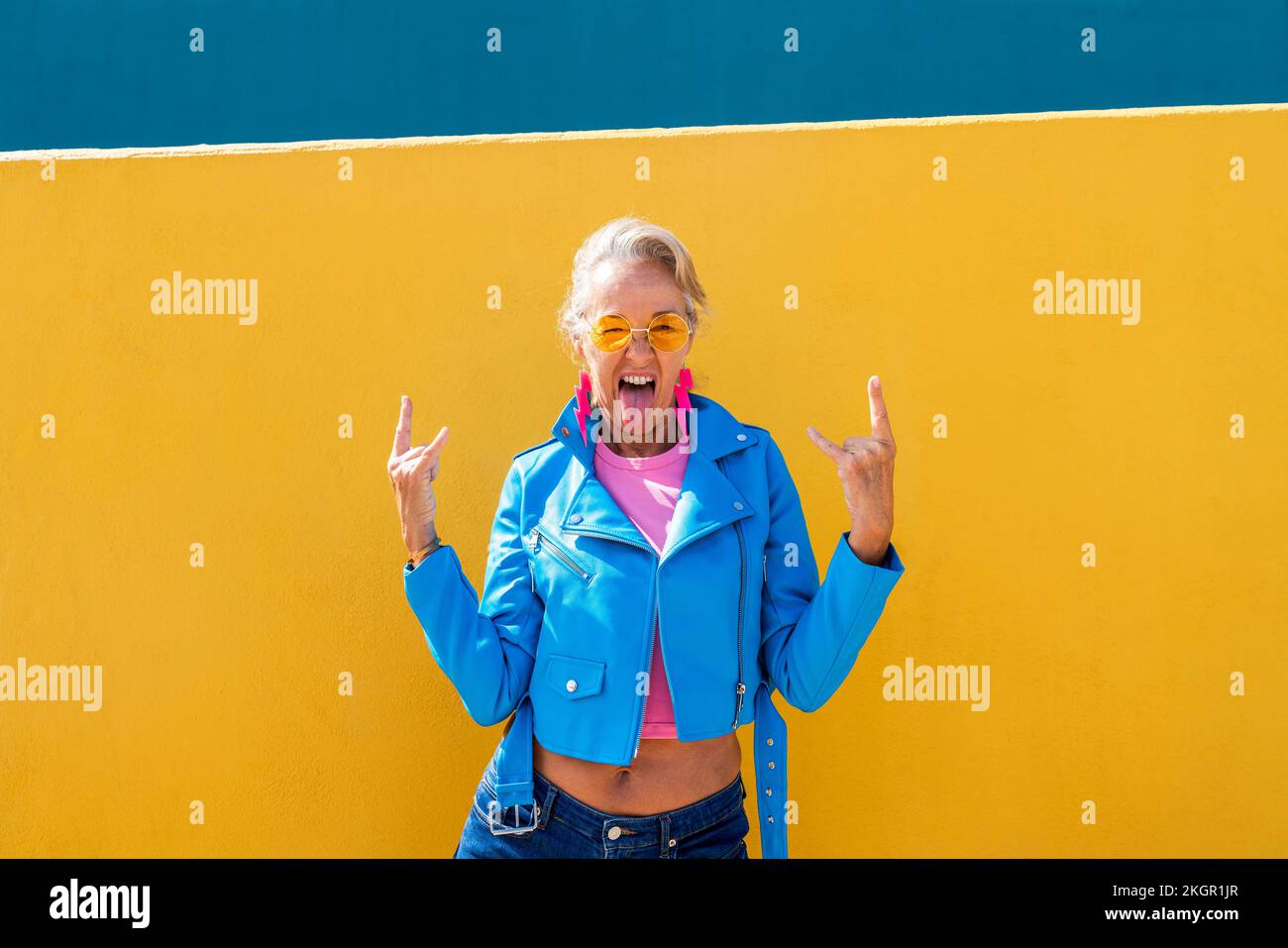 Femme mature qui colle la langue devant le mur coloré Banque D'Images