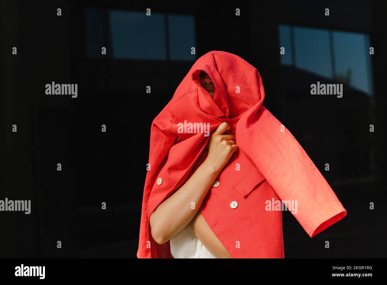 Femme d'affaires couvrant avec blazer rouge devant le mur le jour ensoleillé Banque D'Images