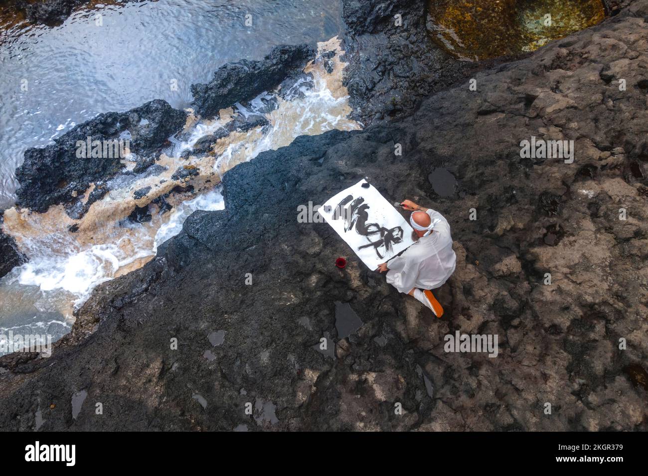 Moine mature faisant de la calligraphie assis sur le rocher par la mer Banque D'Images