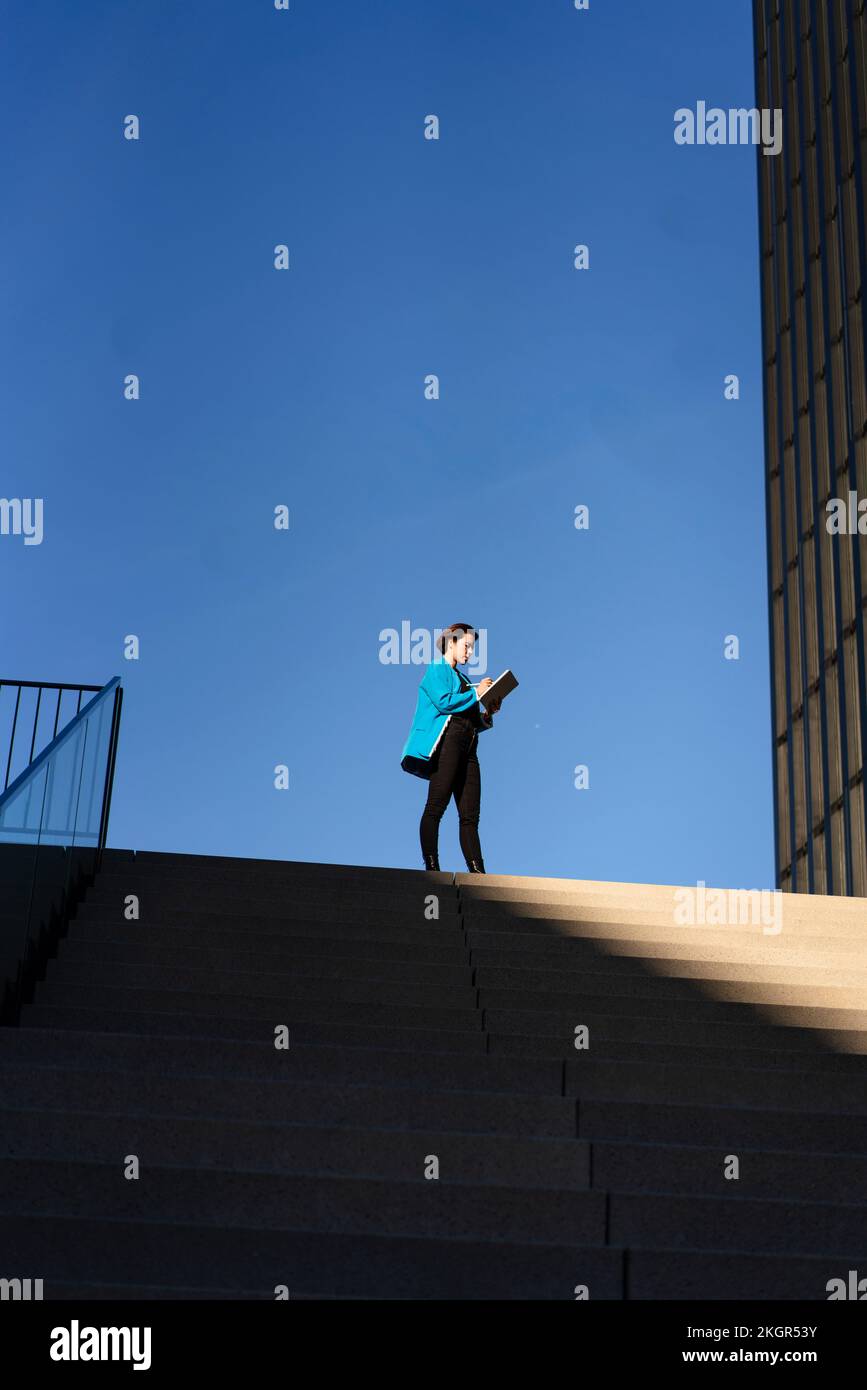 Femme d'affaires debout près des marches avec un ciel bleu clair en arrière-plan Banque D'Images