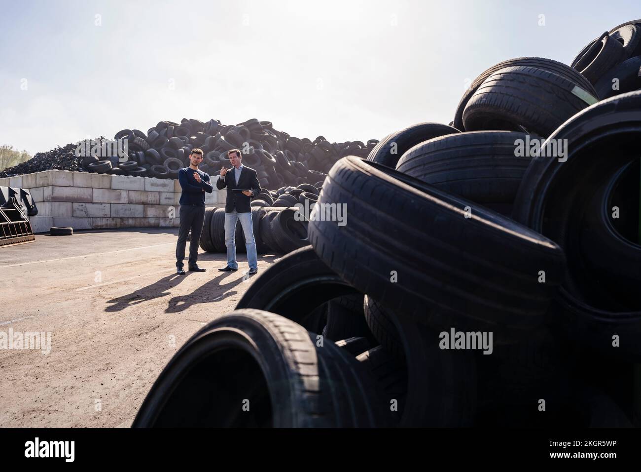 Les hommes d'affaires discutent du tas de pneus en caoutchouc à l'usine de recyclage Banque D'Images