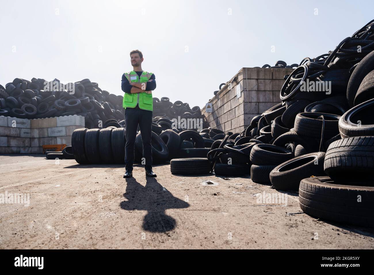 Homme aux bras croisés debout par des pneus à l'usine de recyclage Banque D'Images