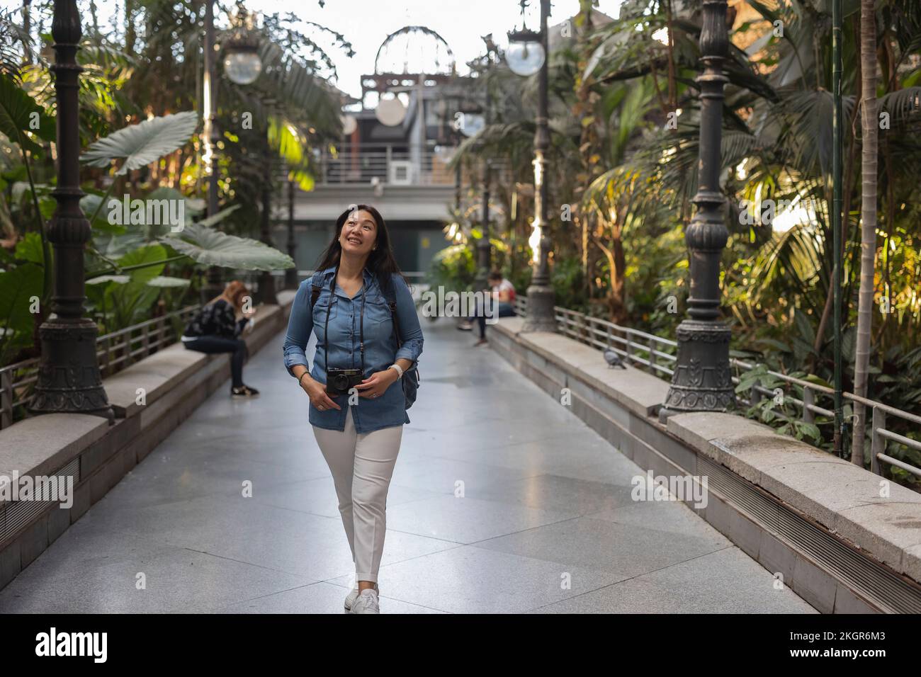 Femme mûre souriante avec caméra marchant sur le sentier dans le parc Banque D'Images