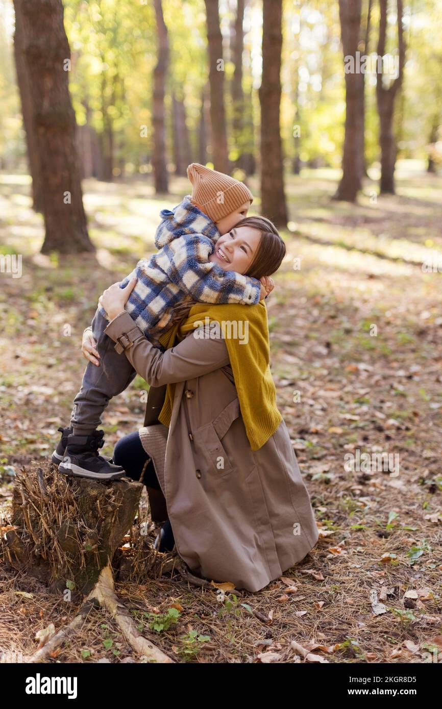 Garçon debout sur une souche d'arbre embrassant la mère dans le parc Banque D'Images