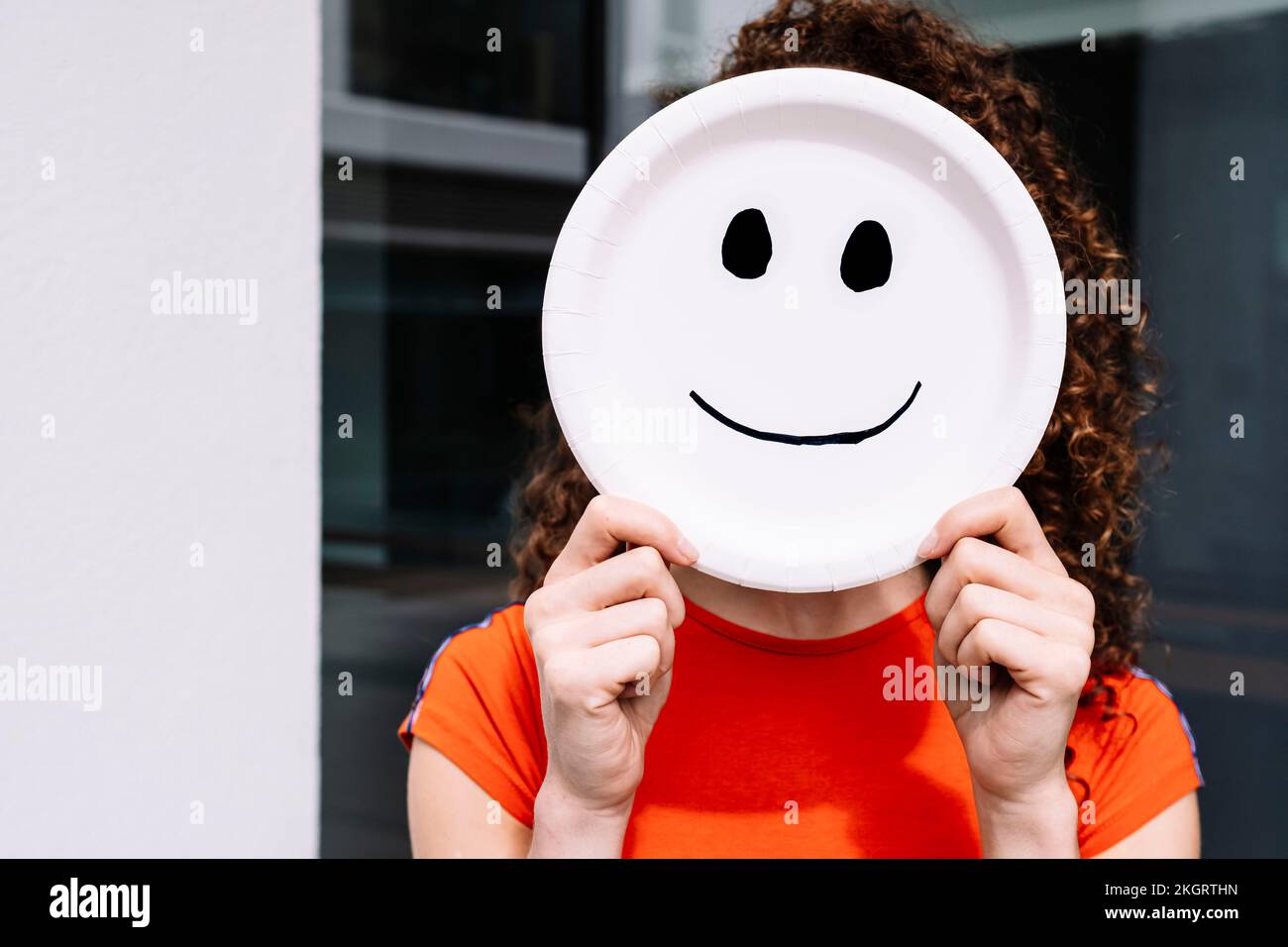 Jeune femme tenant une plaque émoticône souriante sur le visage Banque D'Images