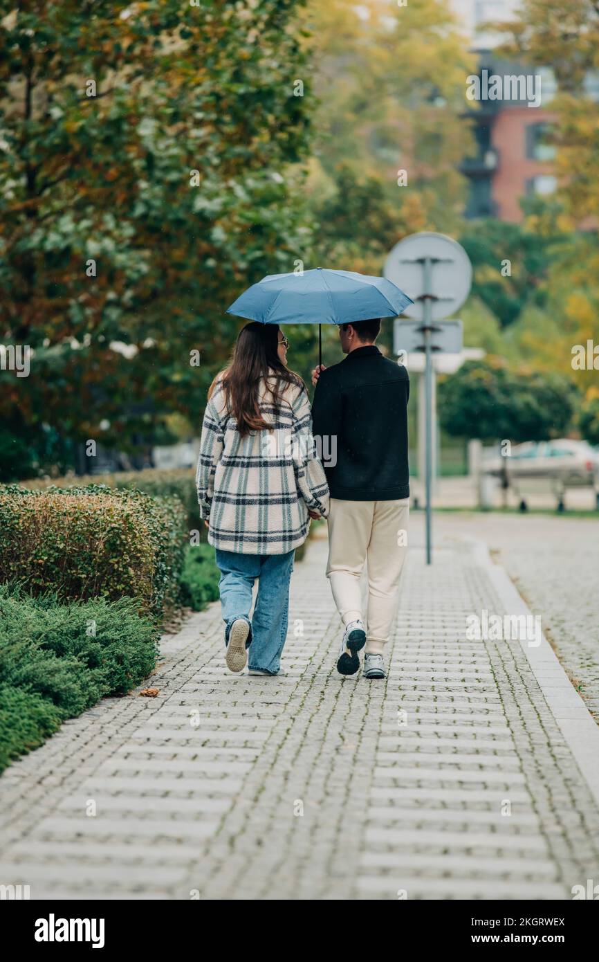 Jeune couple marchant ensemble sous un parapluie sur une piste de marche Banque D'Images Jeune couple marchant ensemble sous un parapluie sur une piste de marche Banque D'Images