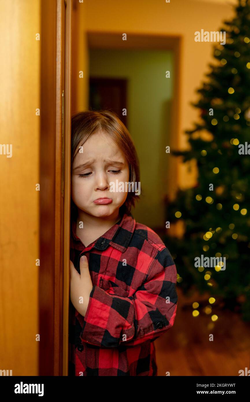 Triste garçon debout près de la porte à la maison Banque D'Images