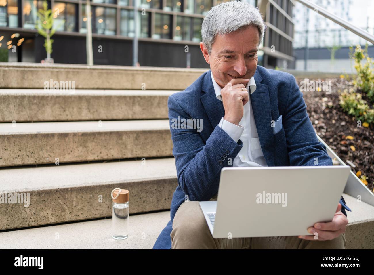 Homme d'affaires mûr regardant un ordinateur portable assis sur des marches Banque D'Images