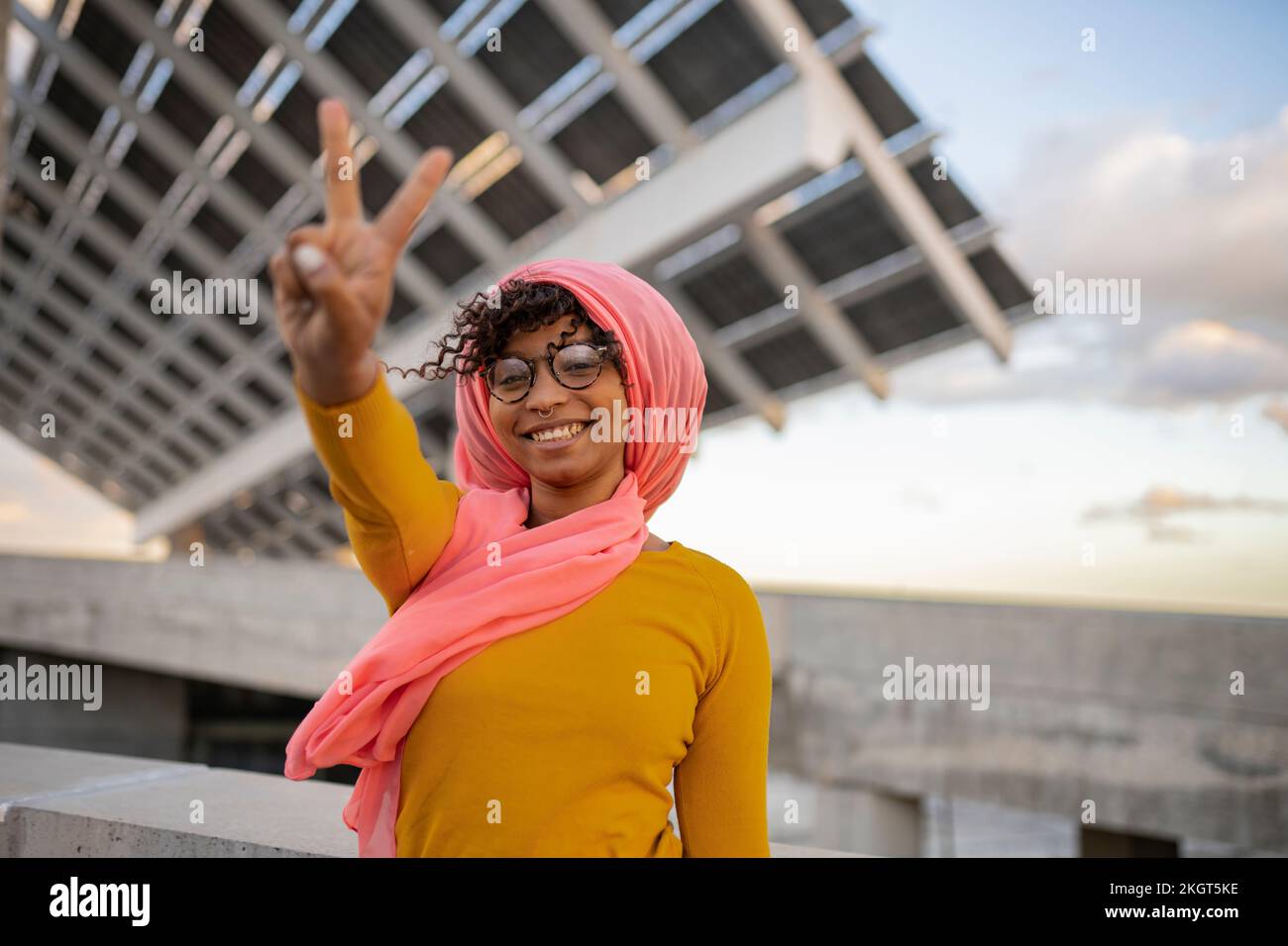Une jeune femme heureuse portant un foulard montrant le signe de la paix geste devant les panneaux Banque D'Images