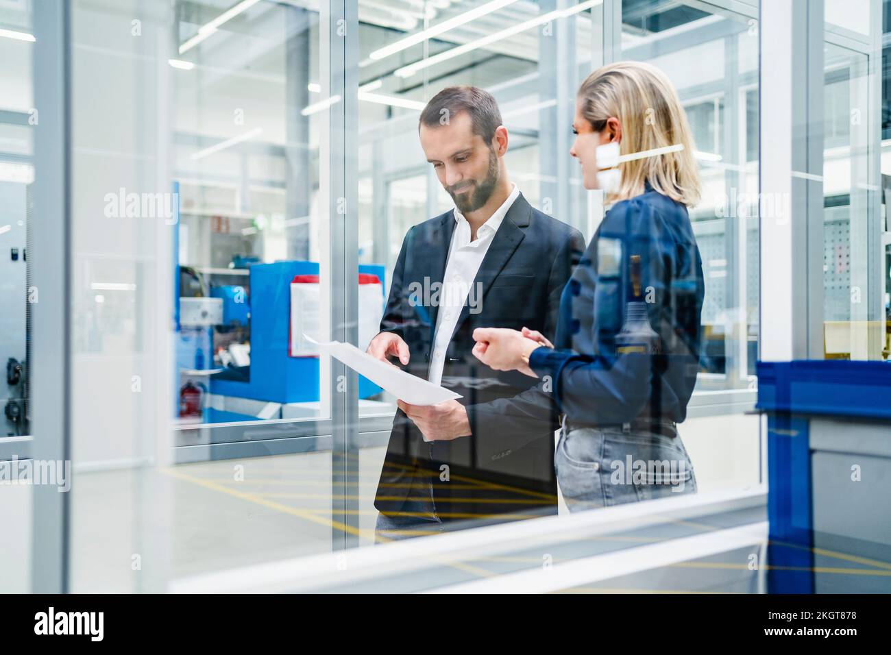 Homme d'affaires examinant des documents avec un collègue en usine vu à travers le verre Banque D'Images