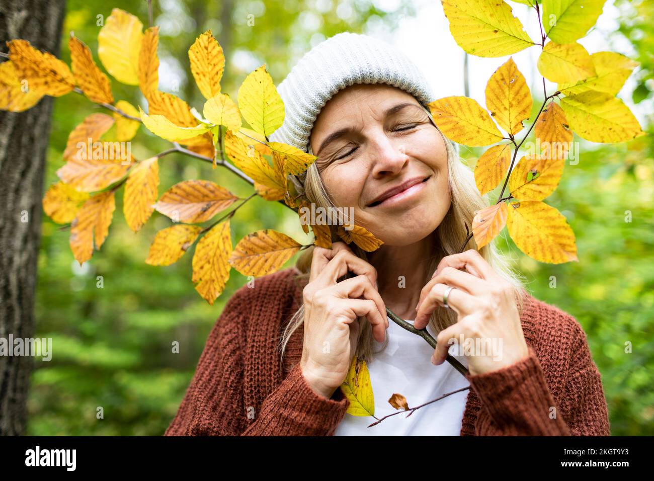 Femme souriante avec les yeux fermés tenant la tige de plante d'automne dans la forêt Banque D'Images