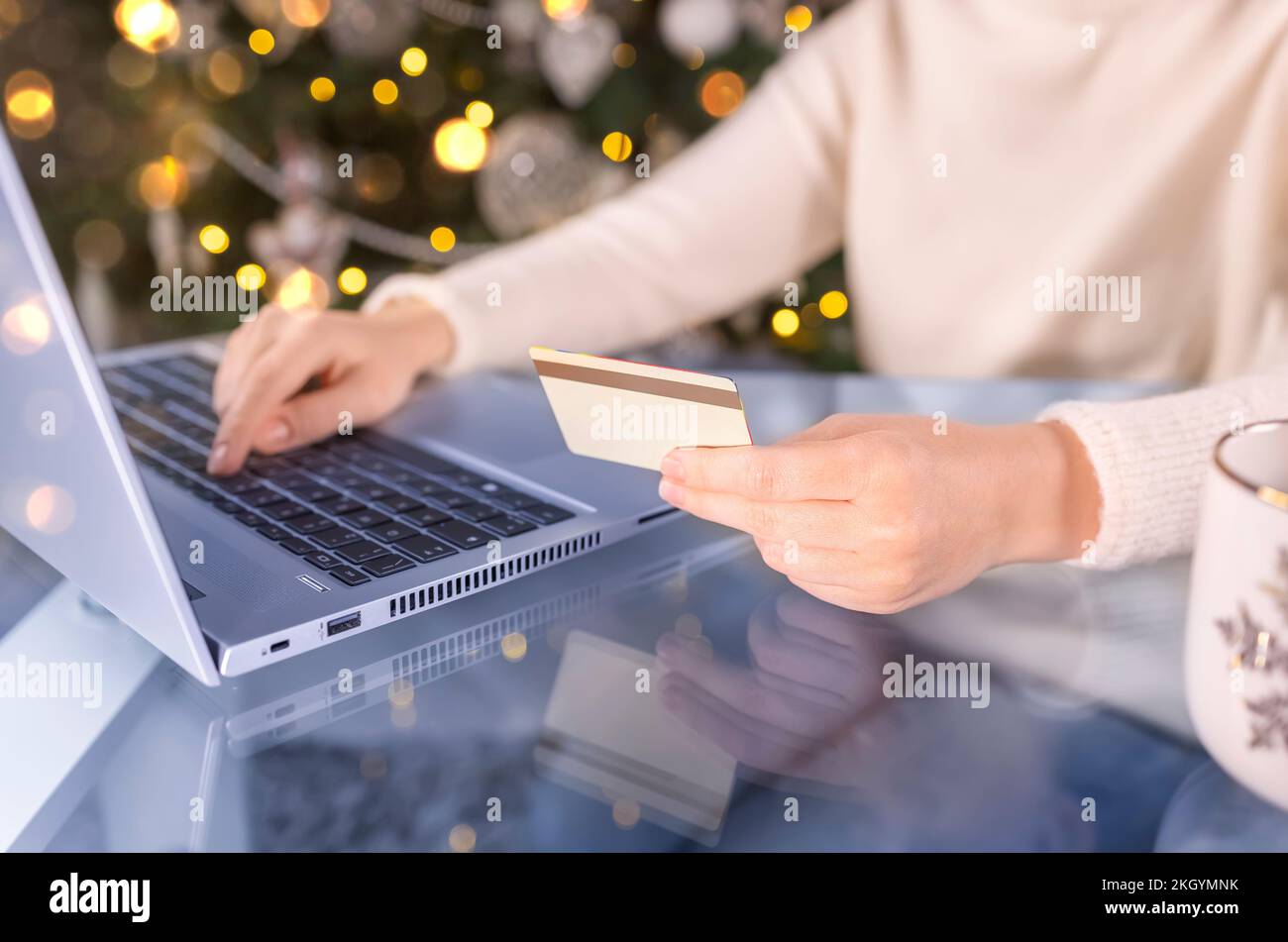 Prise de vue courte des mains de femmes avec carte de crédit dorée et ordinateur portable. Cadeaux de Noël, arbre décoré sur fond. Femme magasiner pour les fêtes p Banque D'Images