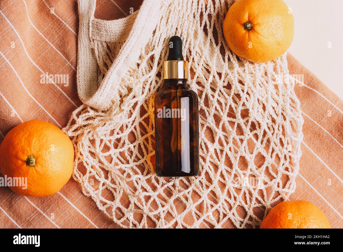 Bouteille de sérum en verre brun sur fond de sac en maille de coton et de mandarines. Produit de beauté biologique. Concept zéro déchet. Vue de dessus. Banque D'Images