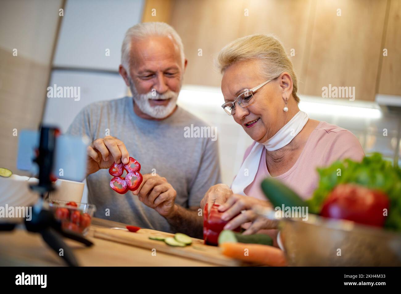 Couple senior enregistrant la vidéo sur la nourriture végétarienne sur la caméra dans la cuisine.Blogging concept. Les gens, la nourriture et les boissons, la technologie et le concept de style de vie Banque D'Images