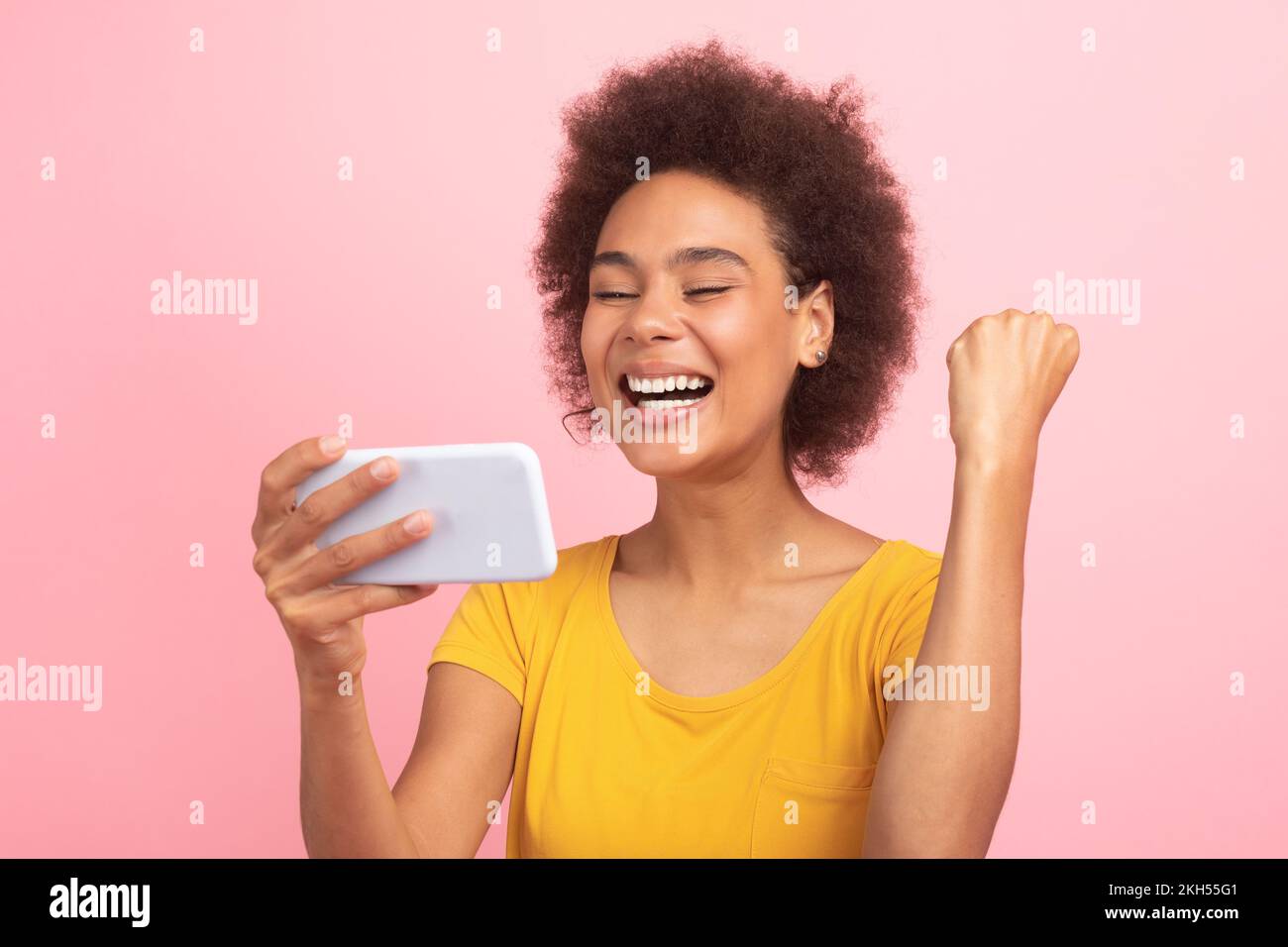 Une jeune femme maurille afro-américaine satisfaite en t-shirt a lu un message sur smartphone, fait le geste de la main de la réussite et de la victoire Banque D'Images