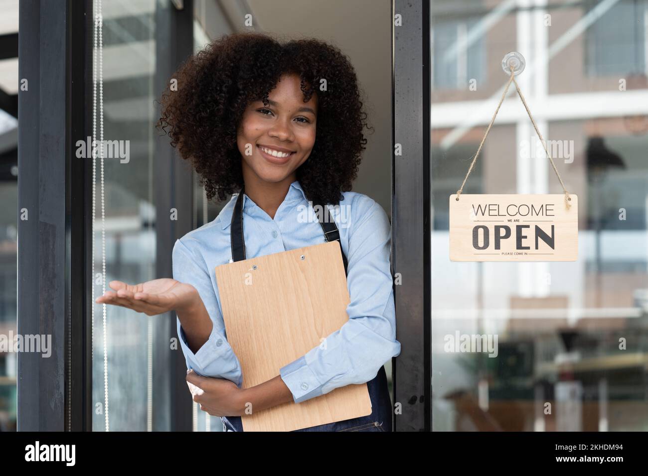 Petite entreprise africaine femme propriétaire souriant tout en tournant le panneau pour l'ouverture du café. Bonne serveuse afro-américaine entrepreneur en tablier présente signe sur Banque D'Images