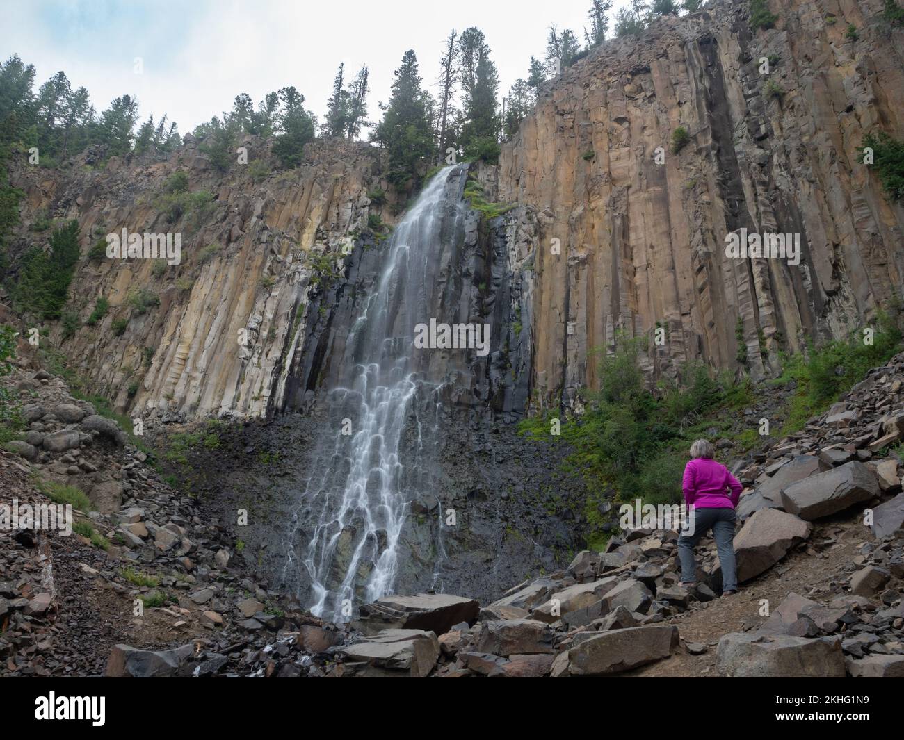 Femme adulte sénior portant une veste fuchsia et un pantalon gris au pied des chutes de Palisade à Hyalite Canyon, Montana, par une journée de fonte. Banque D'Images