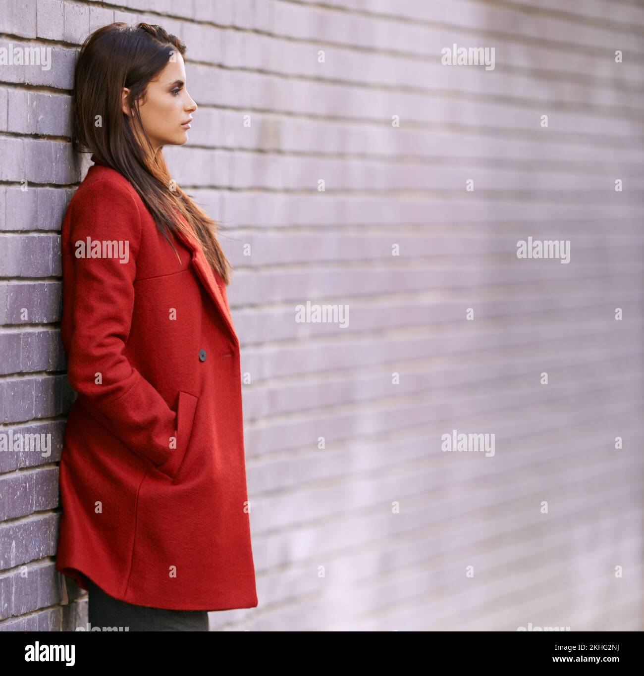 Droite sur la tendance en rouge. une magnifique jeune femme penchée contre un mur de briques dans la ville. Banque D'Images