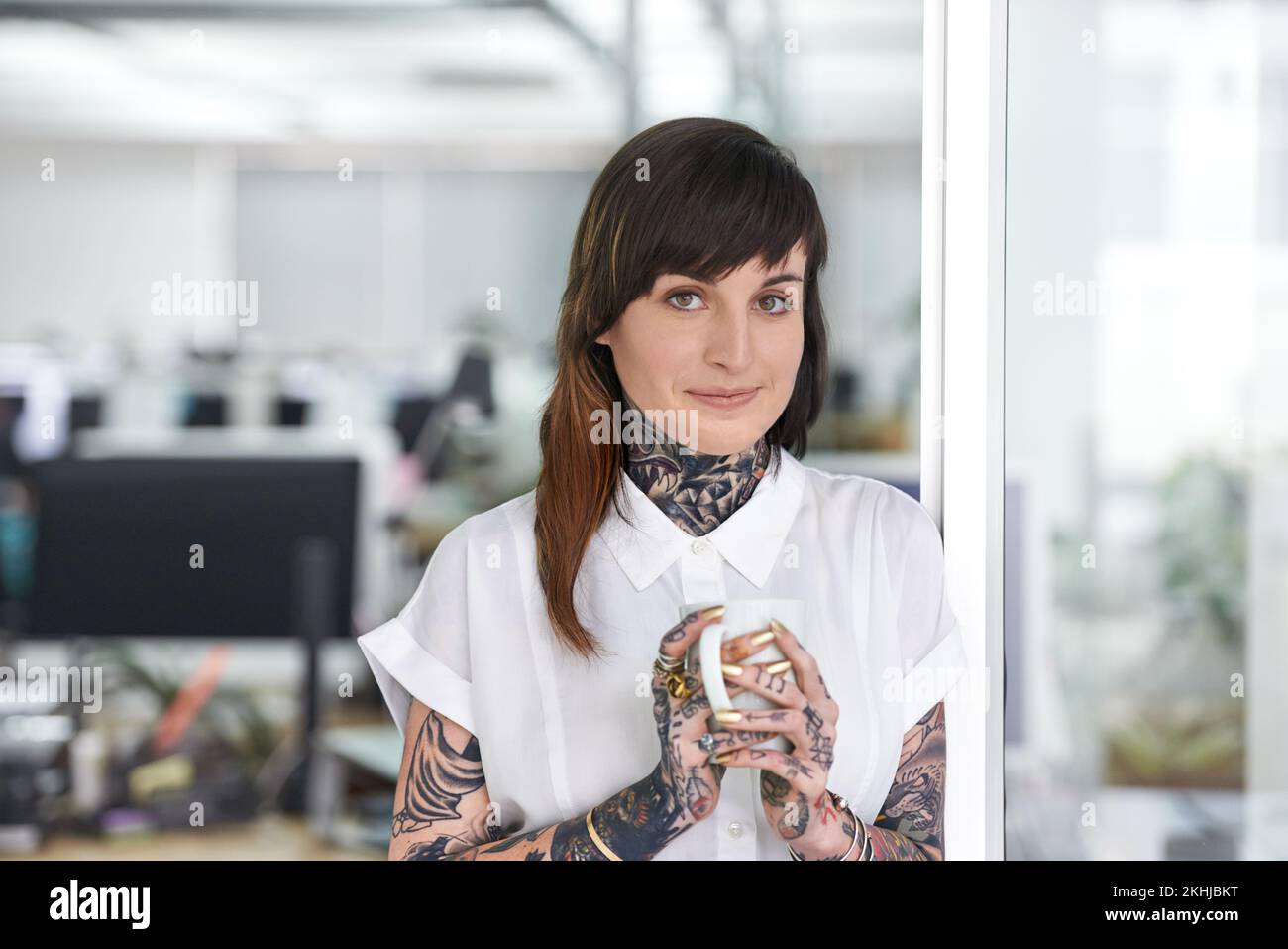 Stéréotypes - qui a besoin de em. Une photo courte d'une femme d'affaires tatouée debout dans son bureau avec une tasse de café. Banque D'Images