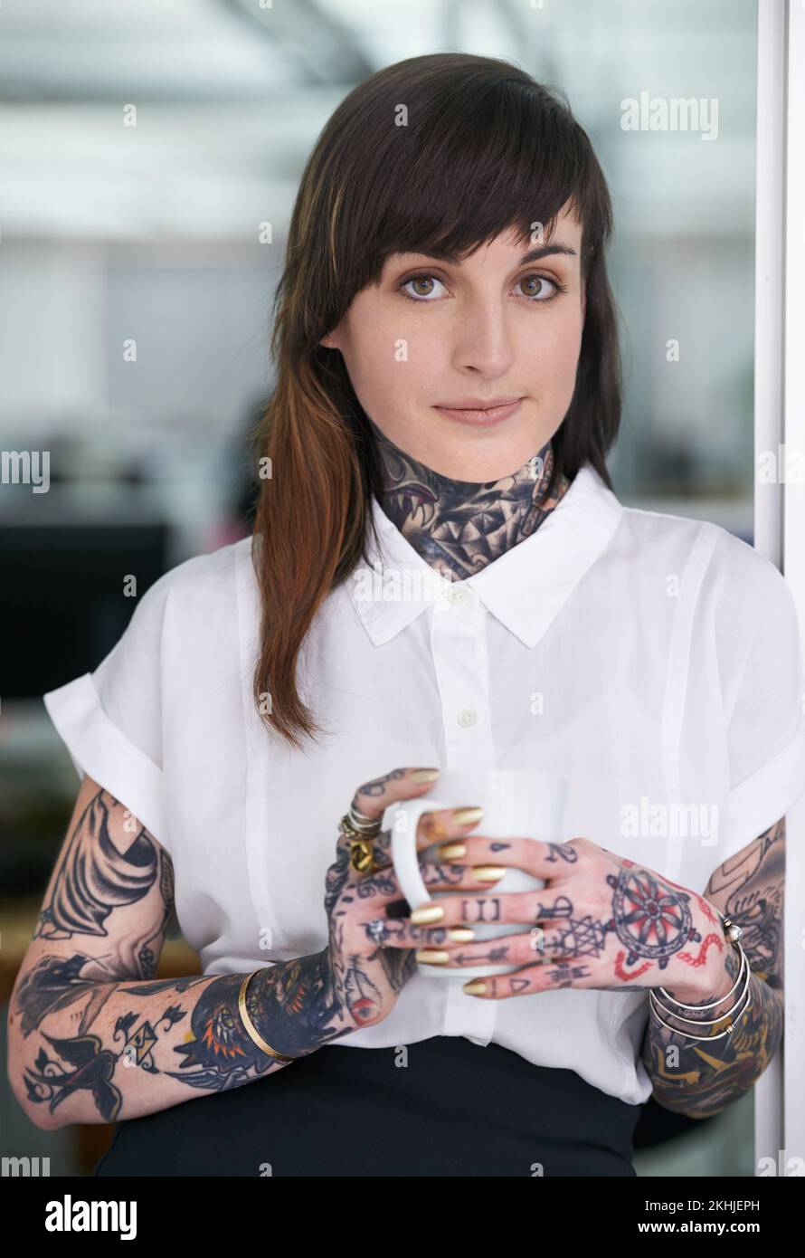 Stéréotypes - qui a besoin de em. Une photo courte d'une femme d'affaires tatouée debout dans son bureau avec une tasse de café. Banque D'Images