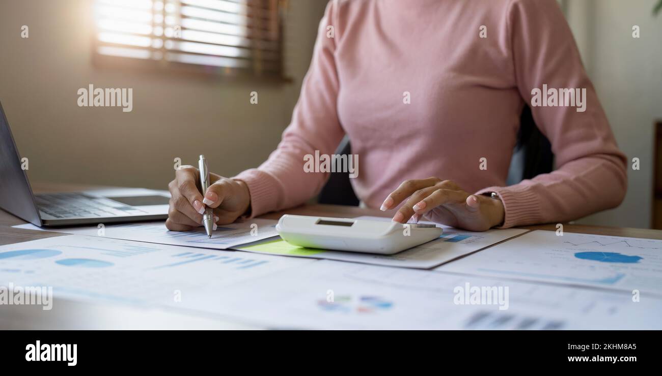 Gros plan d'une femme d'affaires ou d'un comptable tenant le stylo travaillant sur la calculatrice pour calculer les données d'entreprise, le document comptable et l'ordinateur portable à Banque D'Images