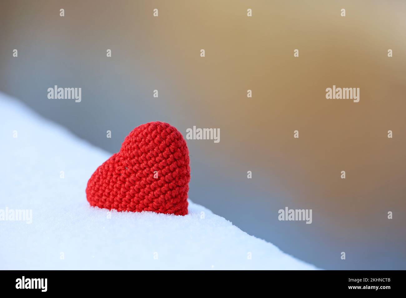 Coeur tricoté rouge dans la neige sur fond flou. Symbole de l'amour romantique, carte de Saint-Valentin Banque D'Images