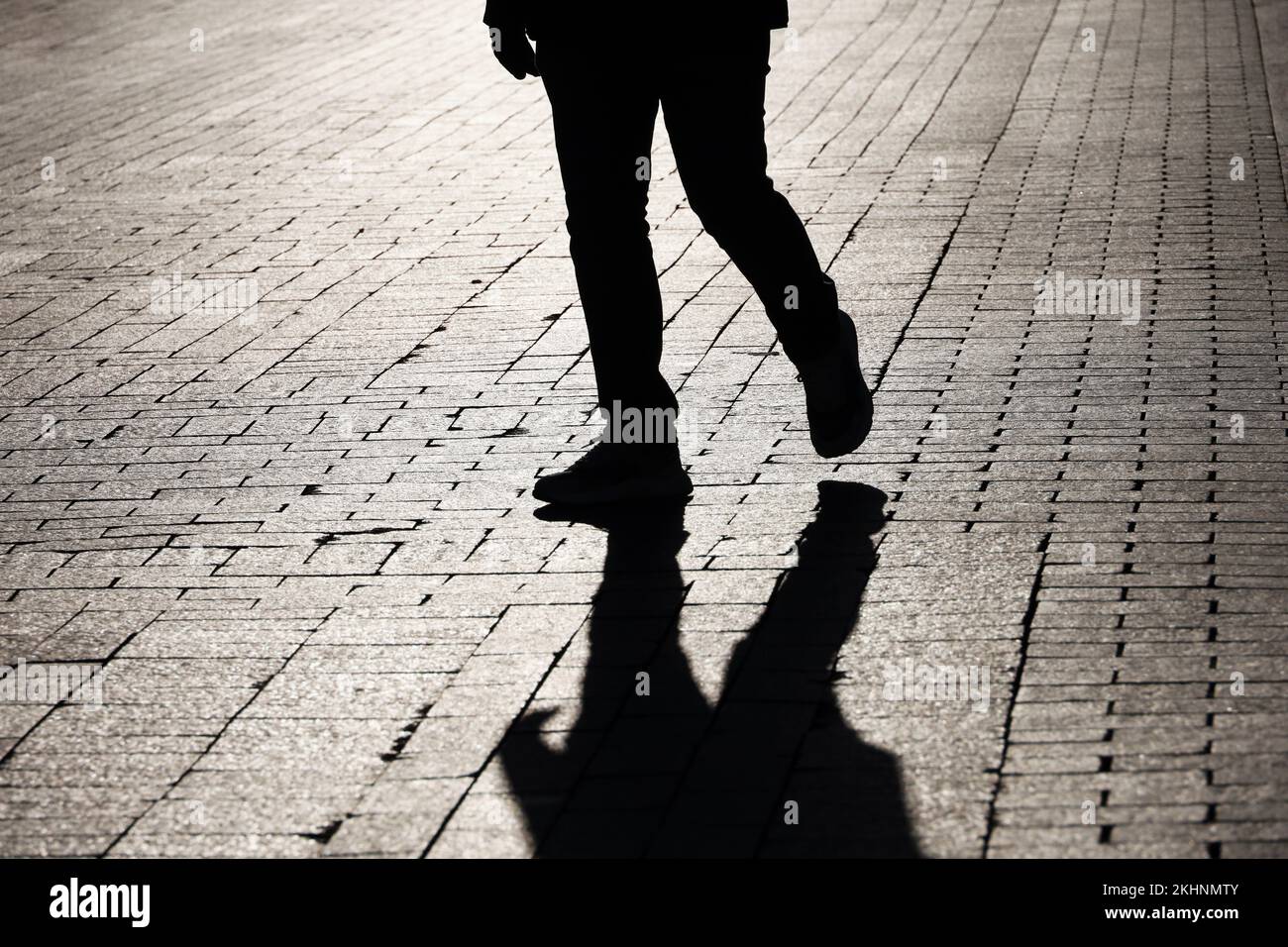 Silhouette noire et ombre d'un homme solitaire qui marche dans une rue. Jambes de sexe masculin en jeans et baskets, vie dramatique Banque D'Images