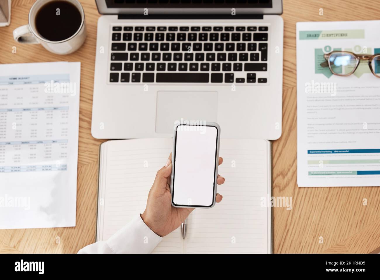 Ordinateur portable, paperasserie et téléphone avec espace de maquette sur un bureau dans un bureau moderne travaillant sur le projet. Tasse de café, ordinateur et main tenant un smartphone Banque D'Images