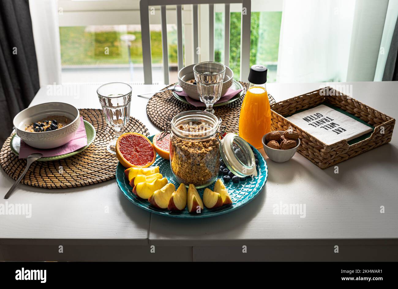 Petit déjeuner sain à l'intérieur avec de délicieux porridge, des tranches de pomme, du pamplemousse coupé, des noisettes et du jus d'orange sur une table en bois blanc près d'une fenêtre ensoleillée Banque D'Images