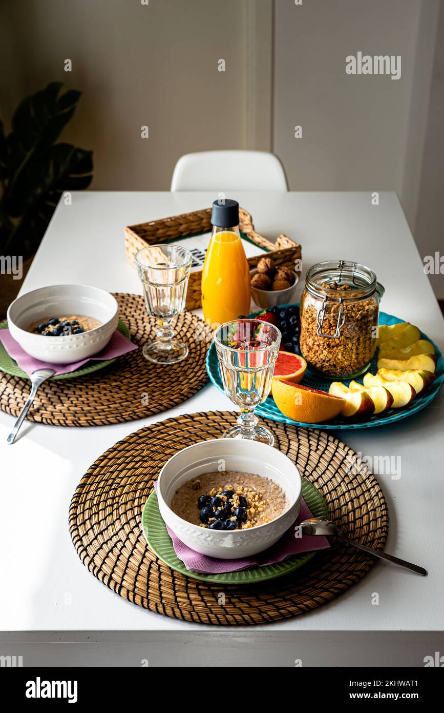 Petit déjeuner frais nourrissant avec porridge, fruits et jus d'orange sur une table intérieure. Repas copieux avec flocons d'avoine et fruits de saison sur un tableau blanc Banque D'Images