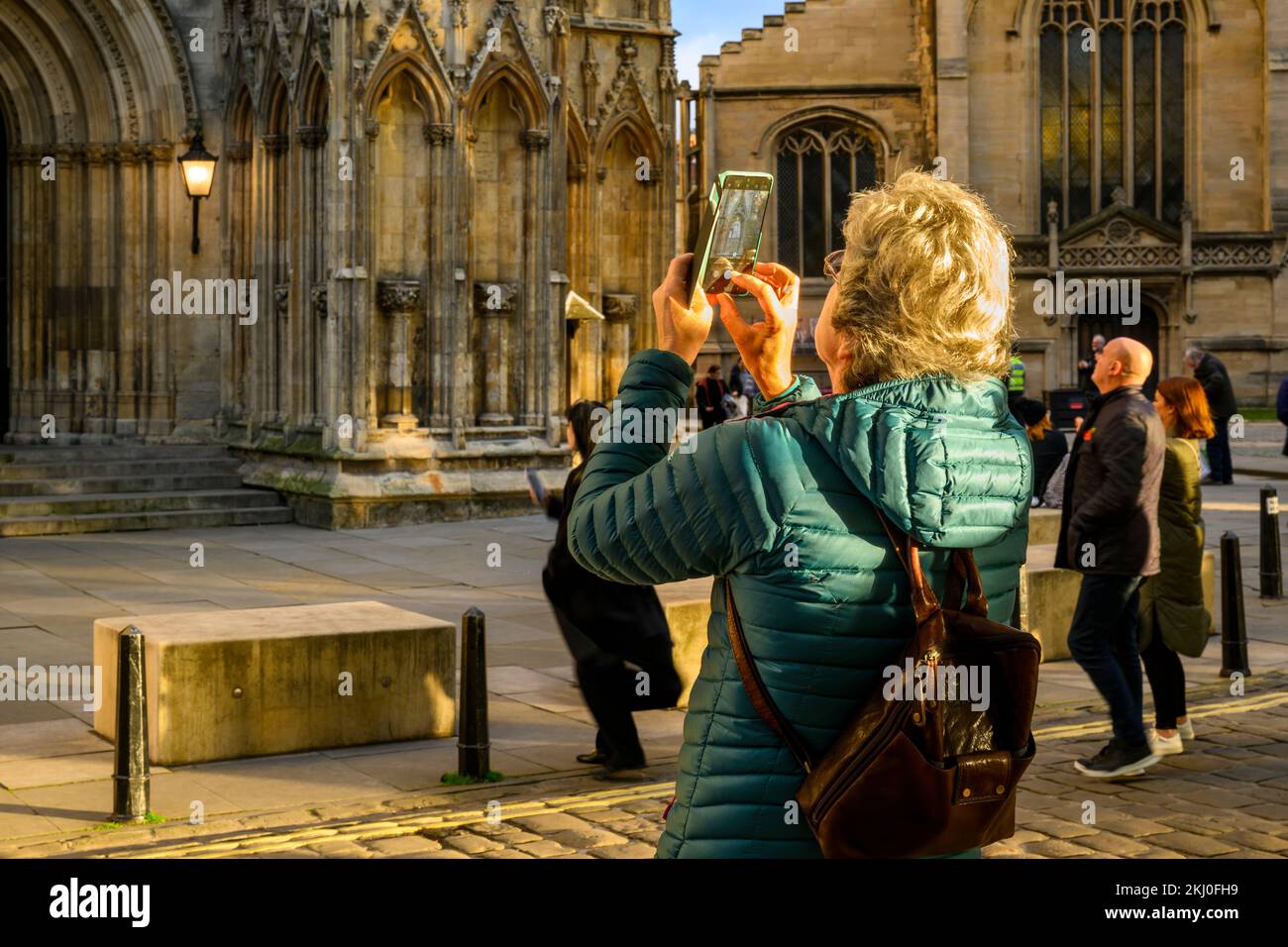Personne utilisant l'appareil photo du téléphone portable (photo de la nouvelle statue Elizabeth 2 sur une niche et visiteurs debout) - York Minster West front, North Yorkshire, Angleterre Royaume-Uni. Banque D'Images