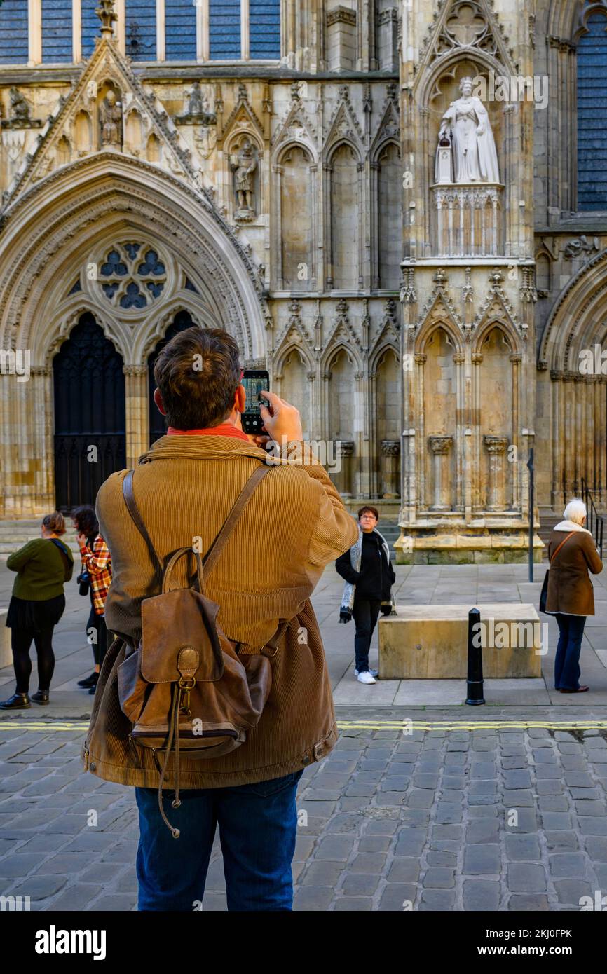Personne utilisant l'appareil photo du téléphone portable (photo de la nouvelle statue Elizabeth 2 sur une niche et visiteurs debout) - York Minster West front, North Yorkshire, Angleterre Royaume-Uni. Banque D'Images