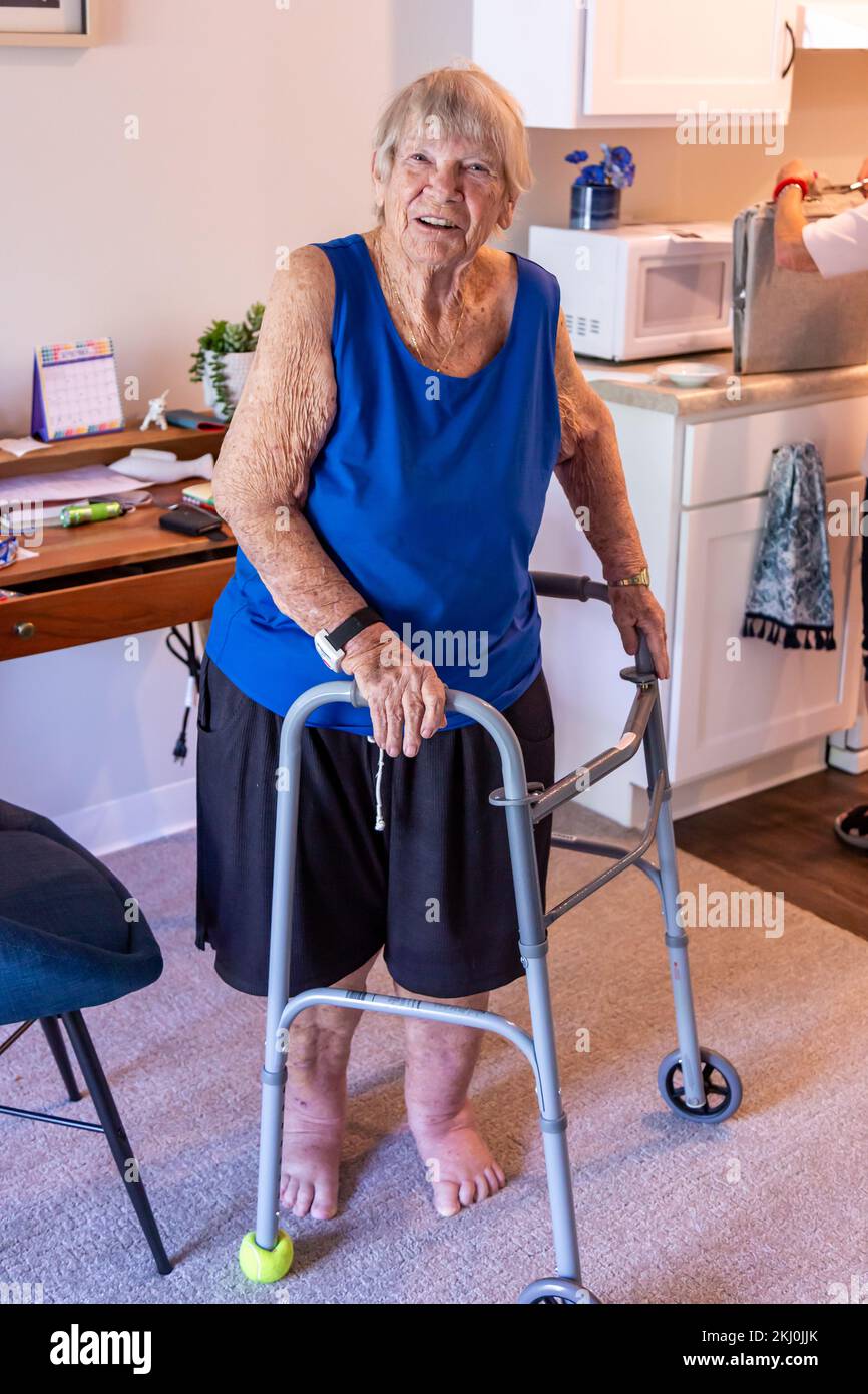 Une femme âgée se tient chez elle avec l'aide d'un marcheur. Banque D'Images