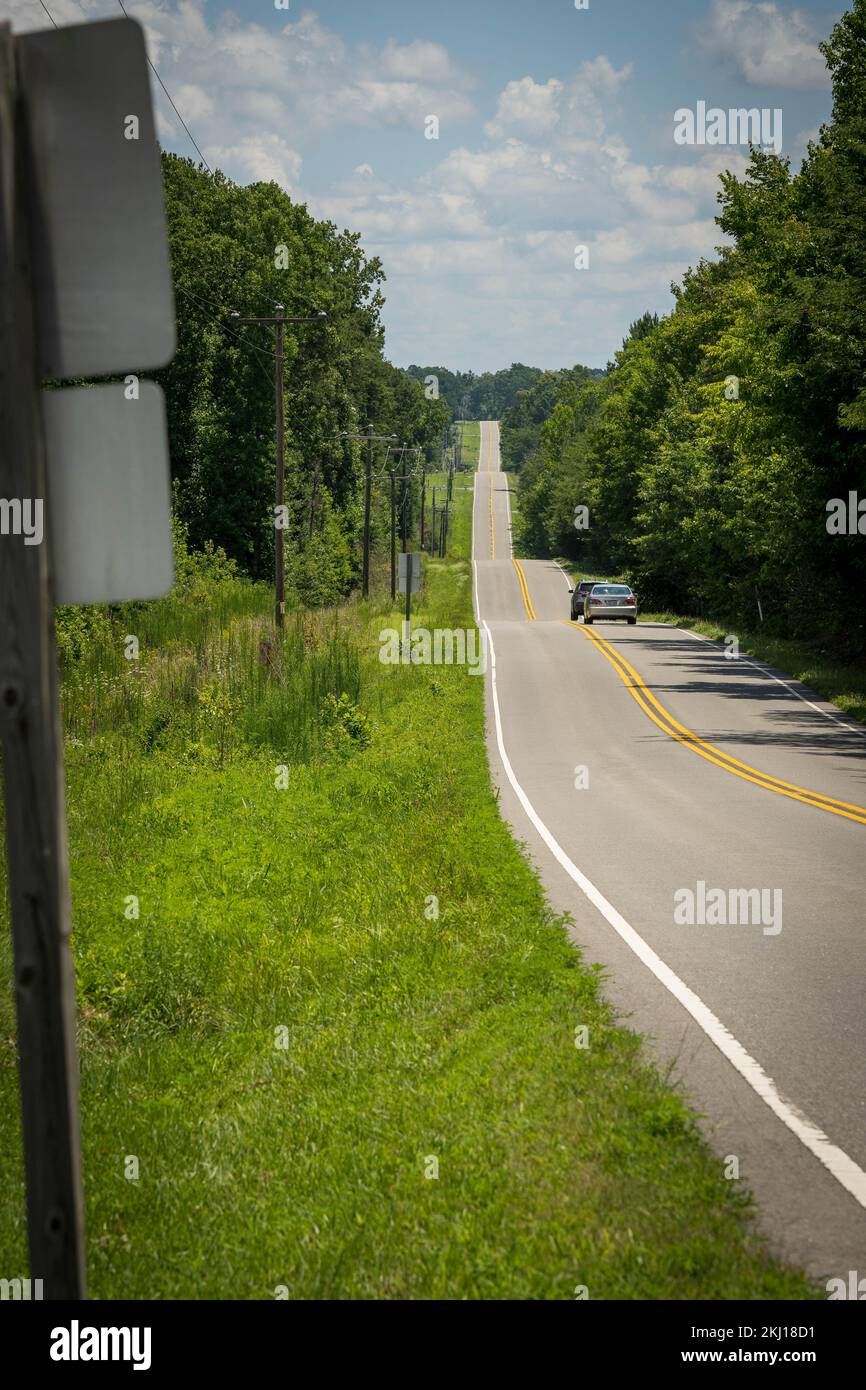 Long chemin d'asphalte droit avec des lignes jaunes et blanches en Amérique, traverse une petite vallée entourée d'arbres et d'herbe Banque D'Images