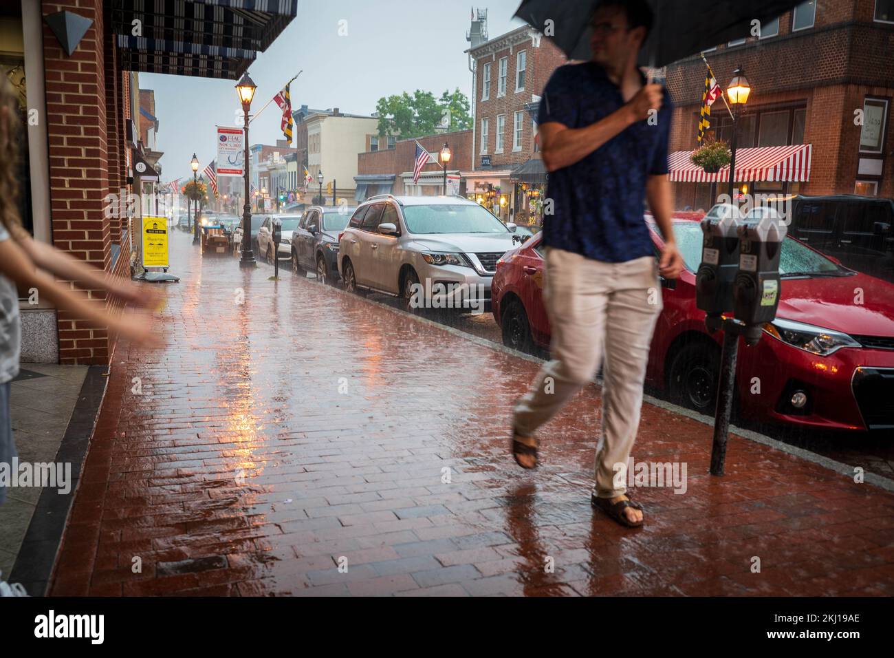 L'homme avec un parapluie marche à travers la douche de pluie dans la rue commerçante et marche après la fille jouant avec ses bras avec les gouttes de pluie Banque D'Images