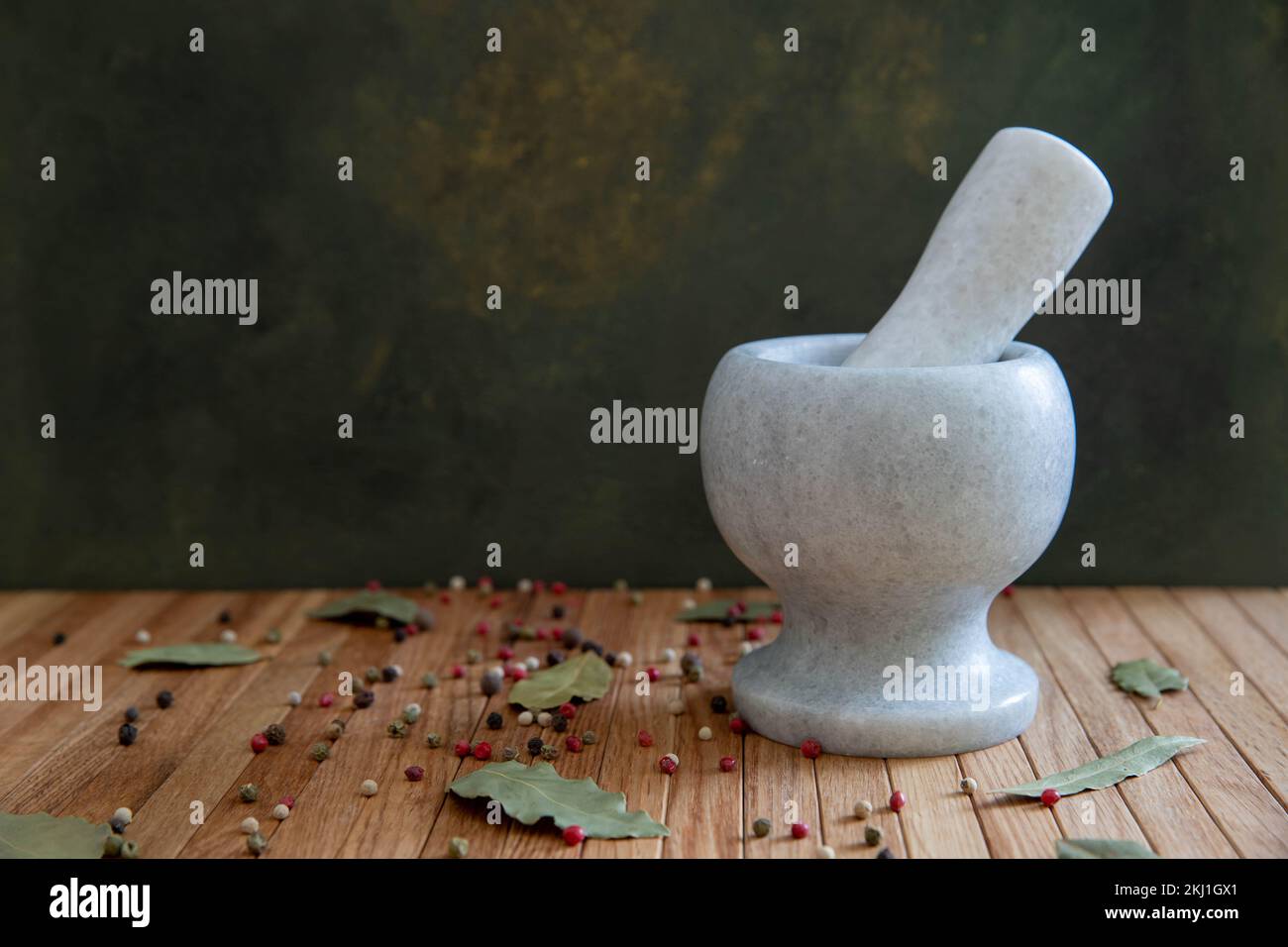 Un mortier en pierre pour épices est posé sur une table en bois sur fond noir. Sur la table se trouvent des feuilles de lavande et un mélange de grains de poivre. Banque D'Images