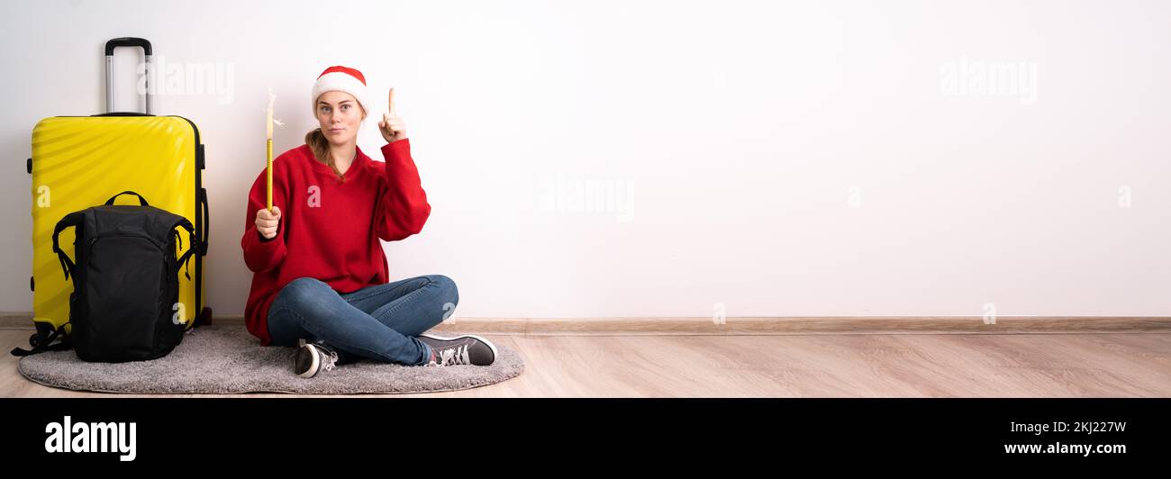 Excitée gaie jeune femme portant chapeau de père Noël assis près de la valise index vers le haut avec grande nouvelle idée regardant caméra isolée sur blanc couleur de dos Banque D'Images